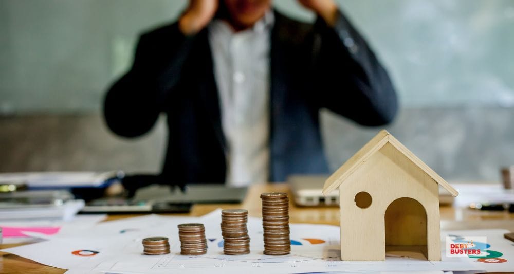 Stacked coins and house model symbolising mortgage stress in Australian families, man stressed in background.