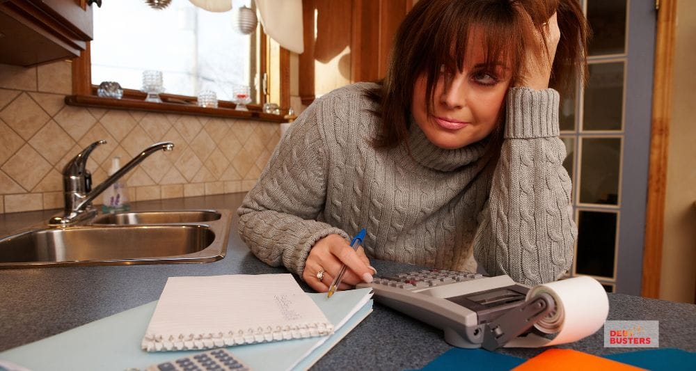 Stressed woman calculating bills at kitchen table, symbolising mortgage stress in Australia families.