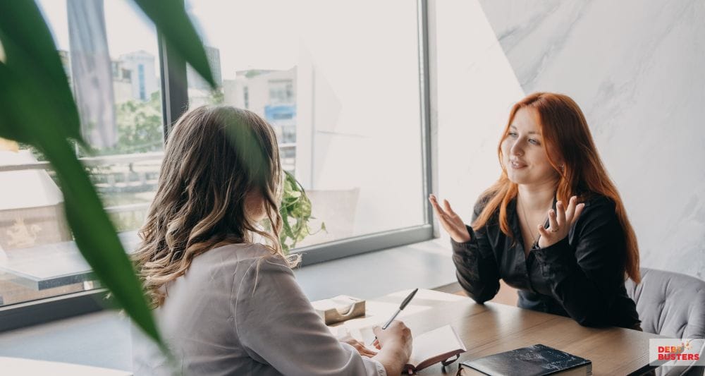 Two women discussing a crisis loan for rent arrears during a financial support meeting.